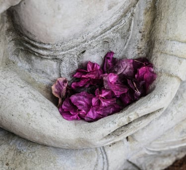 Purple dried flower petals resting in the cupped hands of a stone Buddha statue.