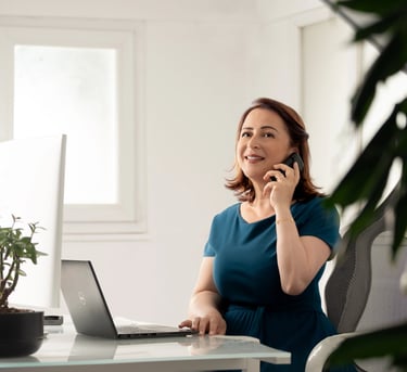 a corporate woman sitting at a desk with a laptop and talking on the phone