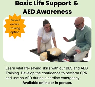 Two people knelt on the floor at the side of a training CPR manikin, defibrillator pads are attached