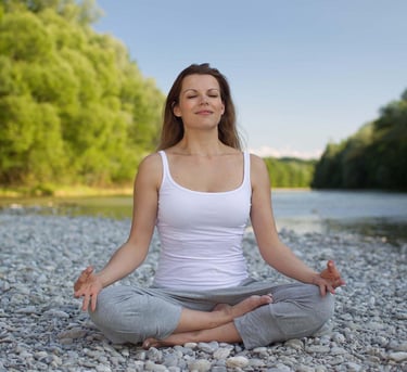 A woman on a lotus pose, sitting by the lake on a bedrock.