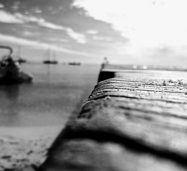 a black and white photo of a pier with boats in the background