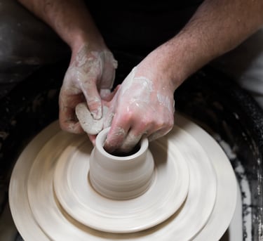 Hands holding a sponge forming a pot on a potter's wheel.