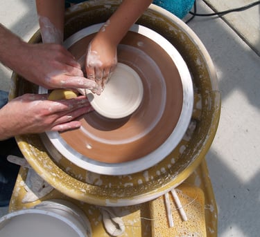 Two hands forming a ceramic bowl on a potter's wheel.