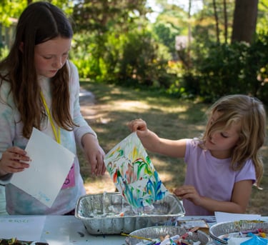 Two young girls lifting pieces of paper from a container to reveal colorful, marbled pieces.