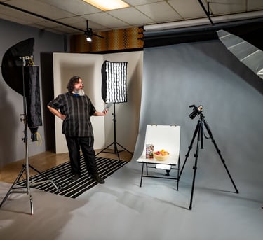 Man standing in a photo studio with equipment including lights, a backdrop, and a camera on a tripod