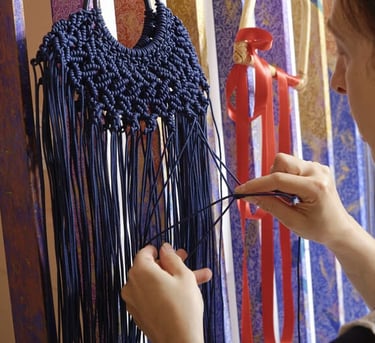 Una mujer anudando un bolso de macramé azul marino hecho a mano con borlas de flecos largos