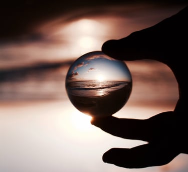 Des doigts tenant une boule de cristal reflétant avec clarté un coucher de soleil sur la mer