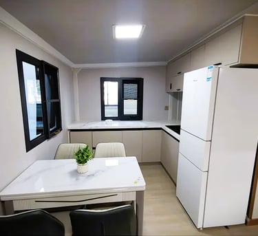 Modern minimalist kitchen with white cabinets, marble dining table, and large white refrigerator.