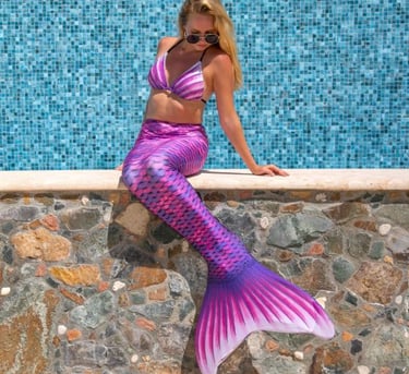 A woman wearing a pink finfun tail. She's sitting on a stone wall, looking down.