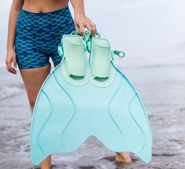 A woman in blue scale-patterned swim shorts. She's holding a light blue monofin.