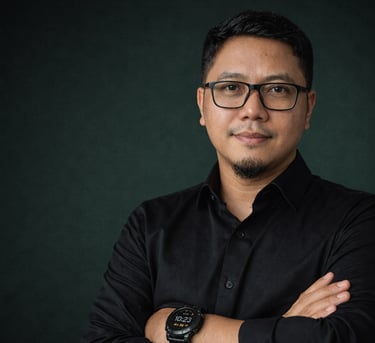 Professional portrait of a man wearing glasses and a black shirt with arms crossed against a dark background.