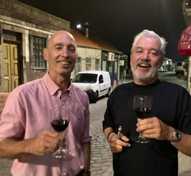 two men standing next to each other holding wine glasses