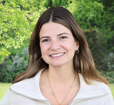 Smiling woman with light brown hair wearing a white sweater in a sunny green park setting.
