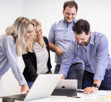 team pinelta standing around a table with a laptop