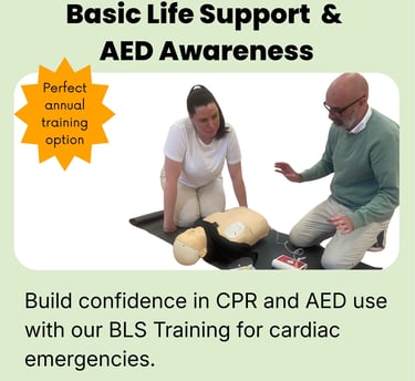 Two people knelt on the floor at the side of a training CPR manikin, defibrillator pads are attached
