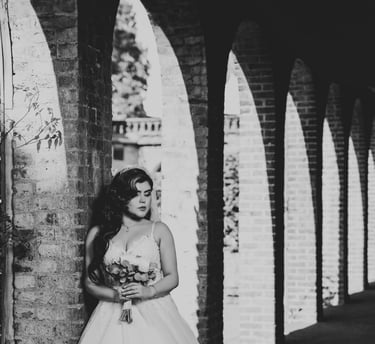 B&W portrait of a bride holding her bouquet under brick arches, photographed by Fred Art Studio.