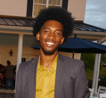 kelvin in a suit and yellow shirt standing in front of a house