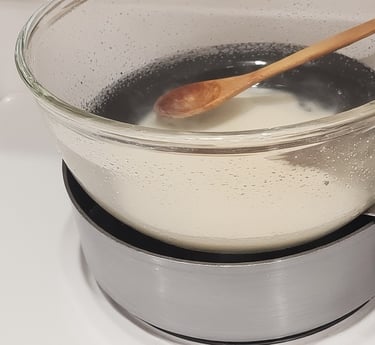 Close-up of glass bowl with melting soap base over a saucepan of water