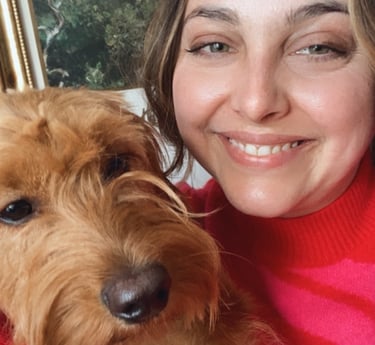 a woman in a hot pink sweater holding a miniature golden doodle with art in the background