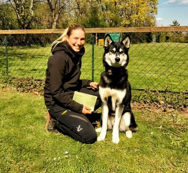 A smiling woman posing with her Alaskan Husky dog at an outdoor obedience training school.
