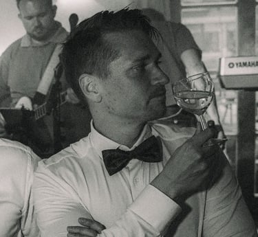 a man in a tuxedo suit drinking a glass of wine