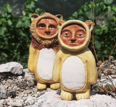 two ceramic figurines, lion and lioness smittie, on a rock in front of a mountain
