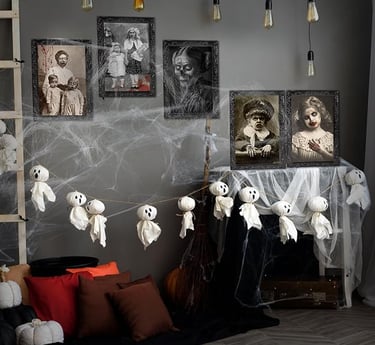 Halloween indoor decoration featuring ghost garland made of fabric hanging across a wall with spider