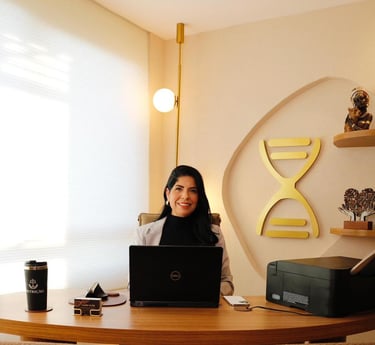 Vanessa Ganime em seu novo consultório sentada na cadeira em uma mesa com o seu laptop.