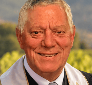 Portrait of a smiling senior wedding officiant wearing a formal stole outdoors.