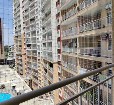 A technician carefully installing a sturdy safety net on a high-rise balcony overlooking Sarjapura R