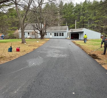 Professional asphalt driveway paving and smoothing for a residential home surrounded by trees.