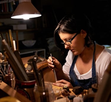 Joyera usando gafas y delantal, trabajando con herramientas manuales para crear joyería