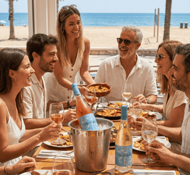 Amigos disfrutando paella con vinos Cola de Gallo en restaurante de playa