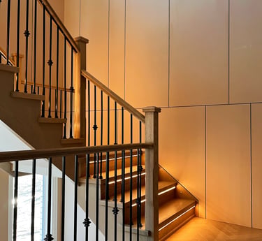 Modern wooden staircase featuring integrated LED tread lighting and black iron balusters.