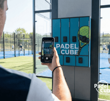 A person using a smartphone to unlock a Padel Cube smart locker at an outdoor padel court facility.