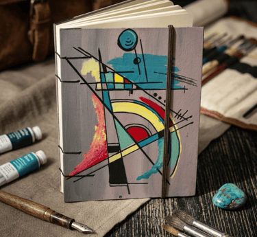 Cuaderno de arte abstracto pintado a mano rodeado de pinceles, tubos de acrílico y plumas