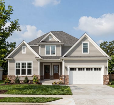 A modern tan craftsman-style home featuring stone accents, a white garage door, and a green lawn.