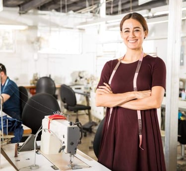 Una diseñadora de moda sonriente, de pie y con los brazos cruzados, en el taller de costura