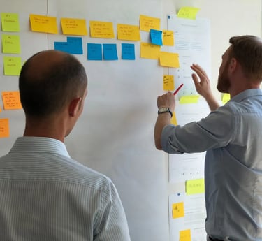 two men standing in front of a white board with sticky notes on it