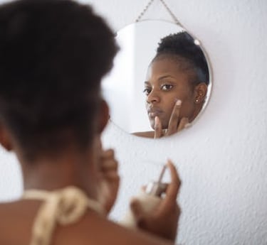 dark skin lady looking in mirror putting cream on spot
