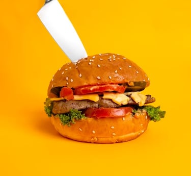 primo piano di un panino burger che viene infilzato da un grosso coltello 
