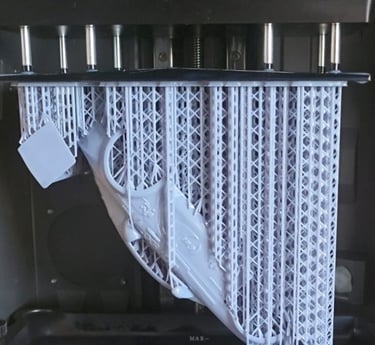 A gray resin 3D printed model with support structures hanging from a build plate inside an SLA 3D printer.