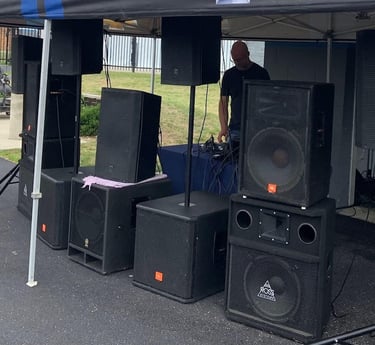 man under a tent behind speakers playing music
