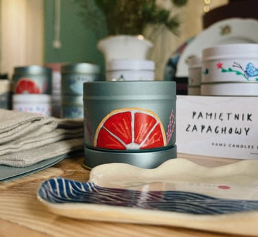 Hand-painted citrus scented candle in a grey metal tin on a wooden table with ceramic dish.