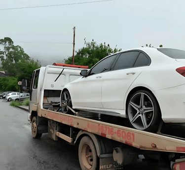 Guincho da Agatão transportando carro de luxo branco em rua úmida e arborizada de Ouro Preto.