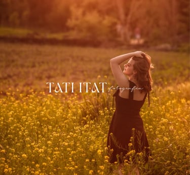 Mulher de vestido preto em campo de flores amarelas ao pôr do sol com o logo da Tati Itat Fotografia