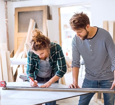 Une femme et un homme en train de mesurer une planche de bois