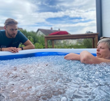 Eine Frau sitzt in tiefer Meditation im Eisbad und wird von einem erfahrenen Wim Hof Instruktor unterstützt