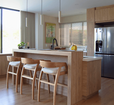 Cocina moderna con acabados en madera clara, isla central y sillas de diseño escandinavo.