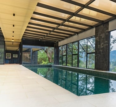 Piscina cubierta rodeada de ventanales, estructura metálica visible y cielo raso de madera.